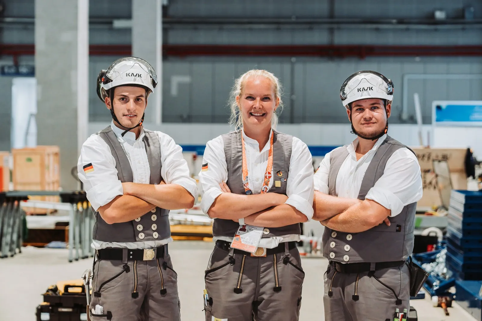 Betonbaumeisterin Jule Janson posiert in einer Werkhalle zwischen Tim Arnold und Jakob Distler. 